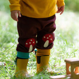 A close up of a child standing in grass and wearing the Little Green Radicals knee patch joggers showing the light blue and yellow leg cuff trim.