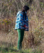 Child wearing a Little Green Radicals blue sun birds recycled waterproof adventure Winter coat with green trousers.