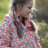 Child wearing Little Green Radicals pink petals recycled waterproof adventure Winter coat. Light coloured coat with an all over pink flower print.