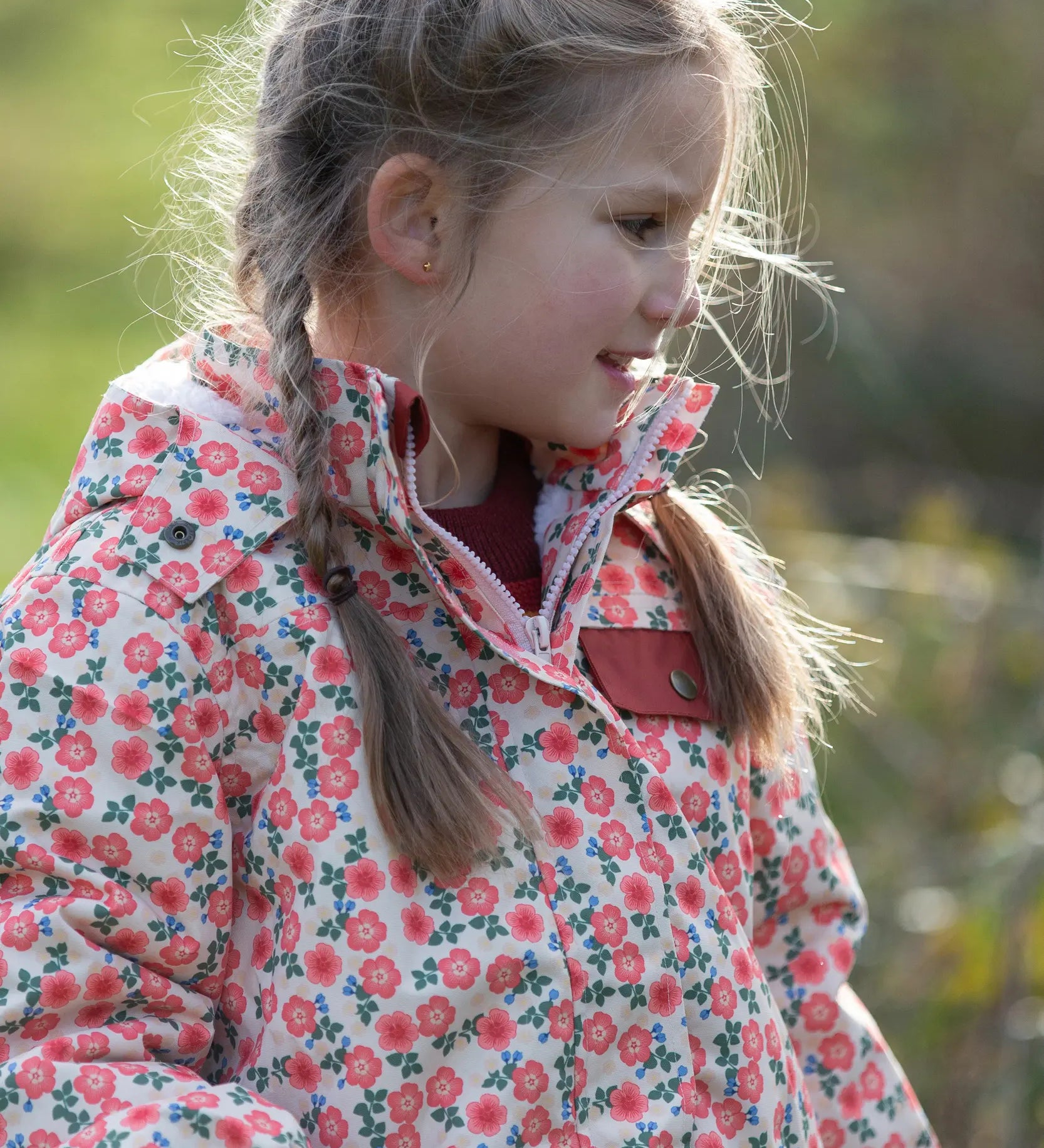 Child wearing Little Green Radicals pink petals recycled waterproof adventure Winter coat. Light coloured coat with an all over pink flower print.