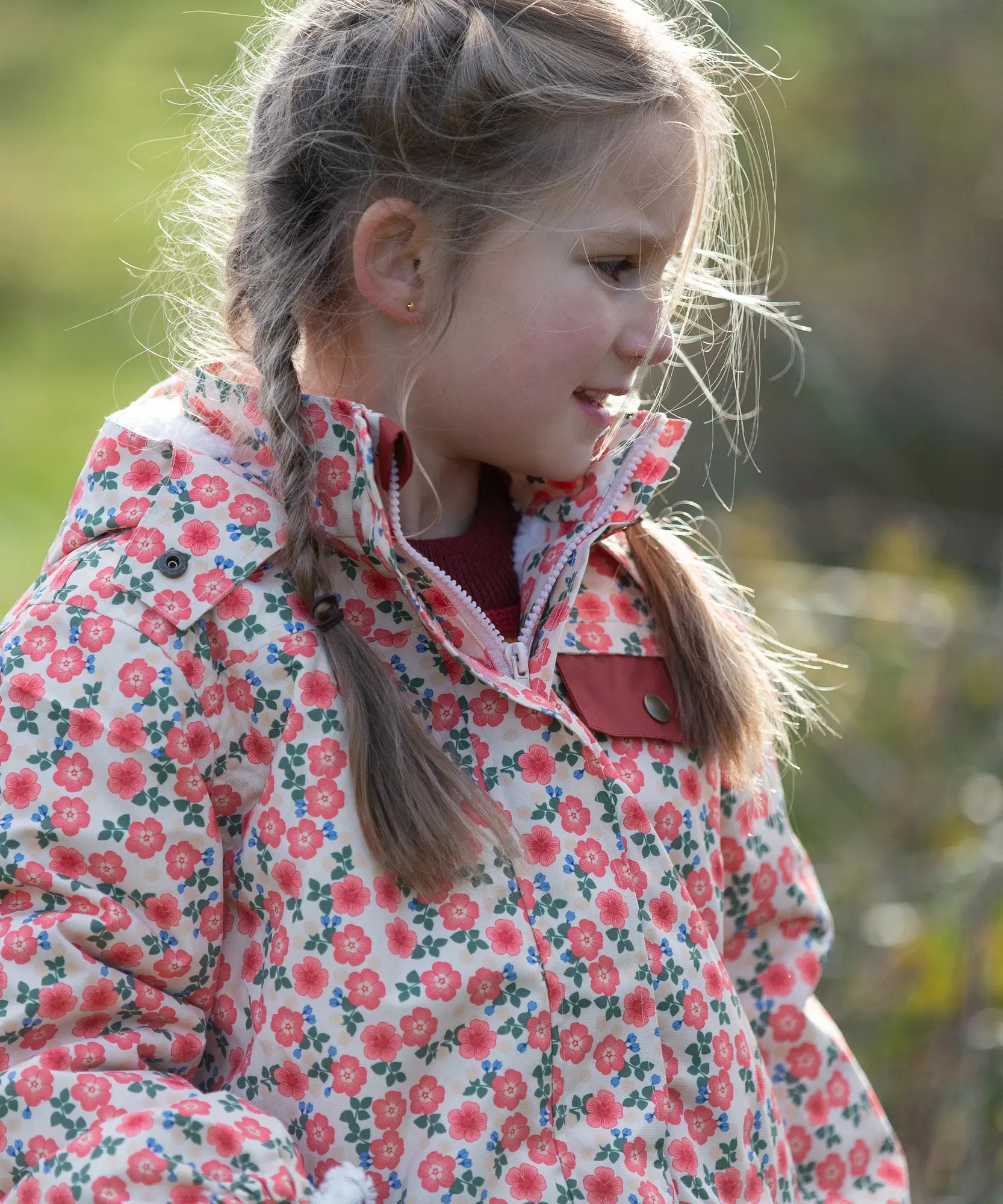 Child wearing Little Green Radicals pink petals recycled waterproof adventure Winter coat. Light coloured coat with an all over pink flower print.