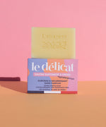 Lamazuna Sensitive Skin Soap Bar, on top of its packaging box, on a pink and orange background
