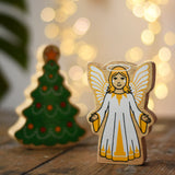 Lanka Kade Christmas angel toy, a wooden figure printed on both sides, next to a Lanka Kade Christmas tree.