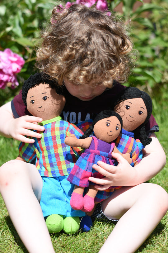 Young boy with blonde curly hair cuddling 3 Lanka Kade fair trade dolls with brown skin, black hair in colourful clothes made from recycled saris to represent Lanka Kade fair trade dolls at Babipur, official UK stockist.