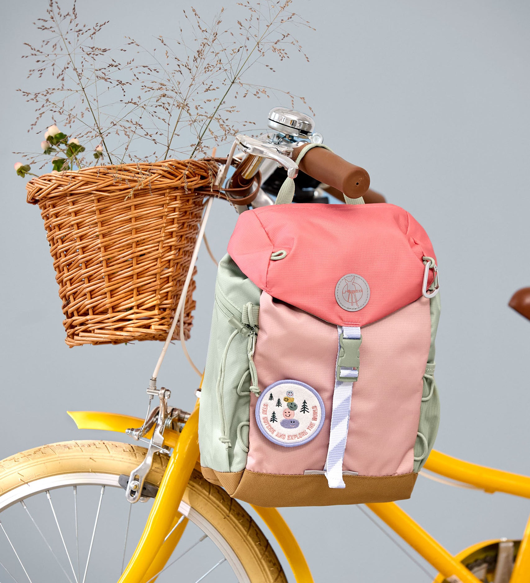 Lassig kids mini outdoor backpack in sunny explorer pink hanging on a yellow bicycle. 
