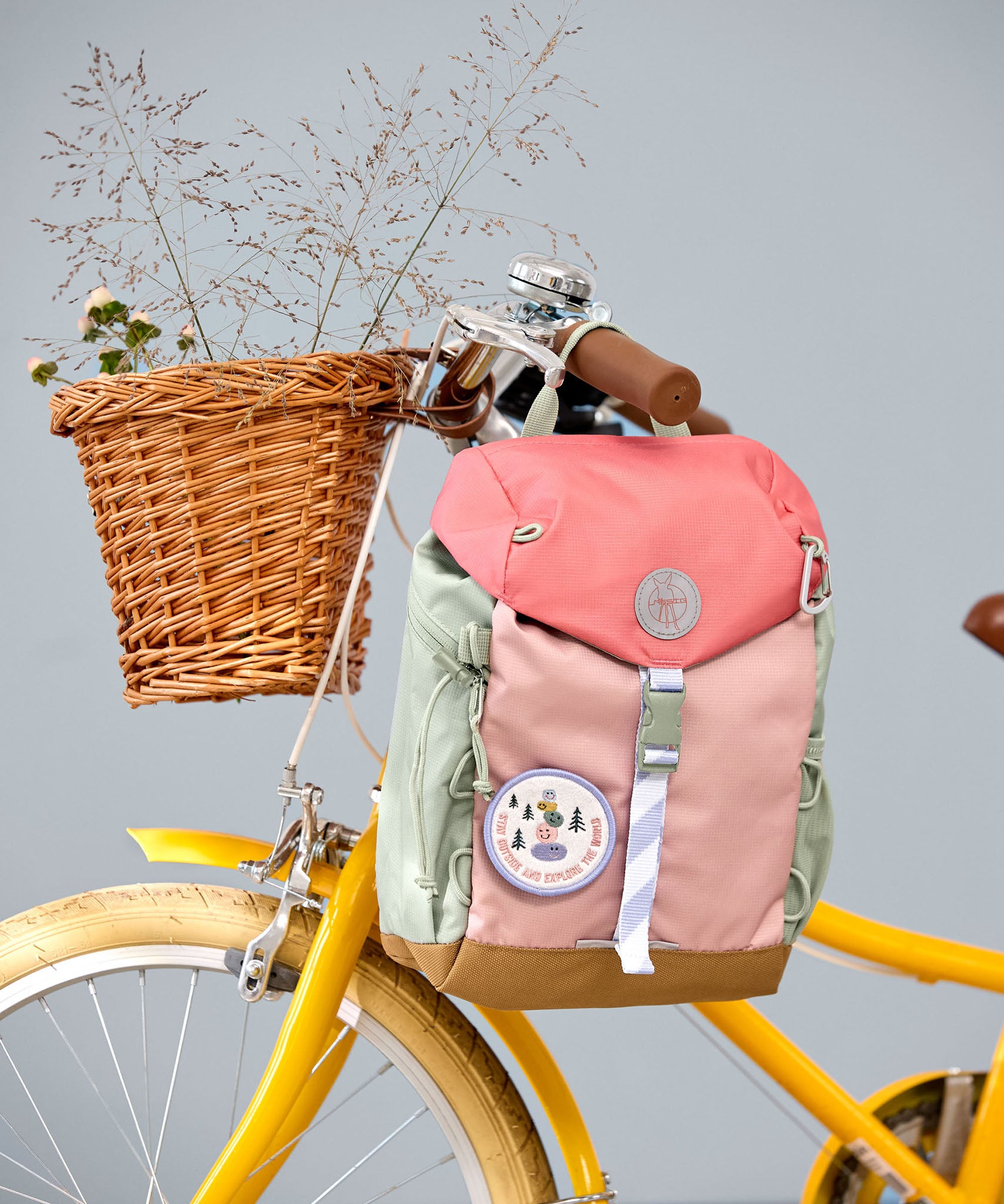 Lassig kids mini outdoor backpack in sunny explorer pink hanging on a yellow bicycle. 