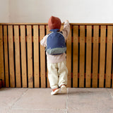 A small child standing near a wooden fence and wearing the Lassig kids tiny backpack in whale 