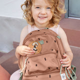 A child sitting outside and holding the Lassig kids mini happy prints Caramel pattern backpack. A pale brown backpack with a cute horse patch on the front panel. 