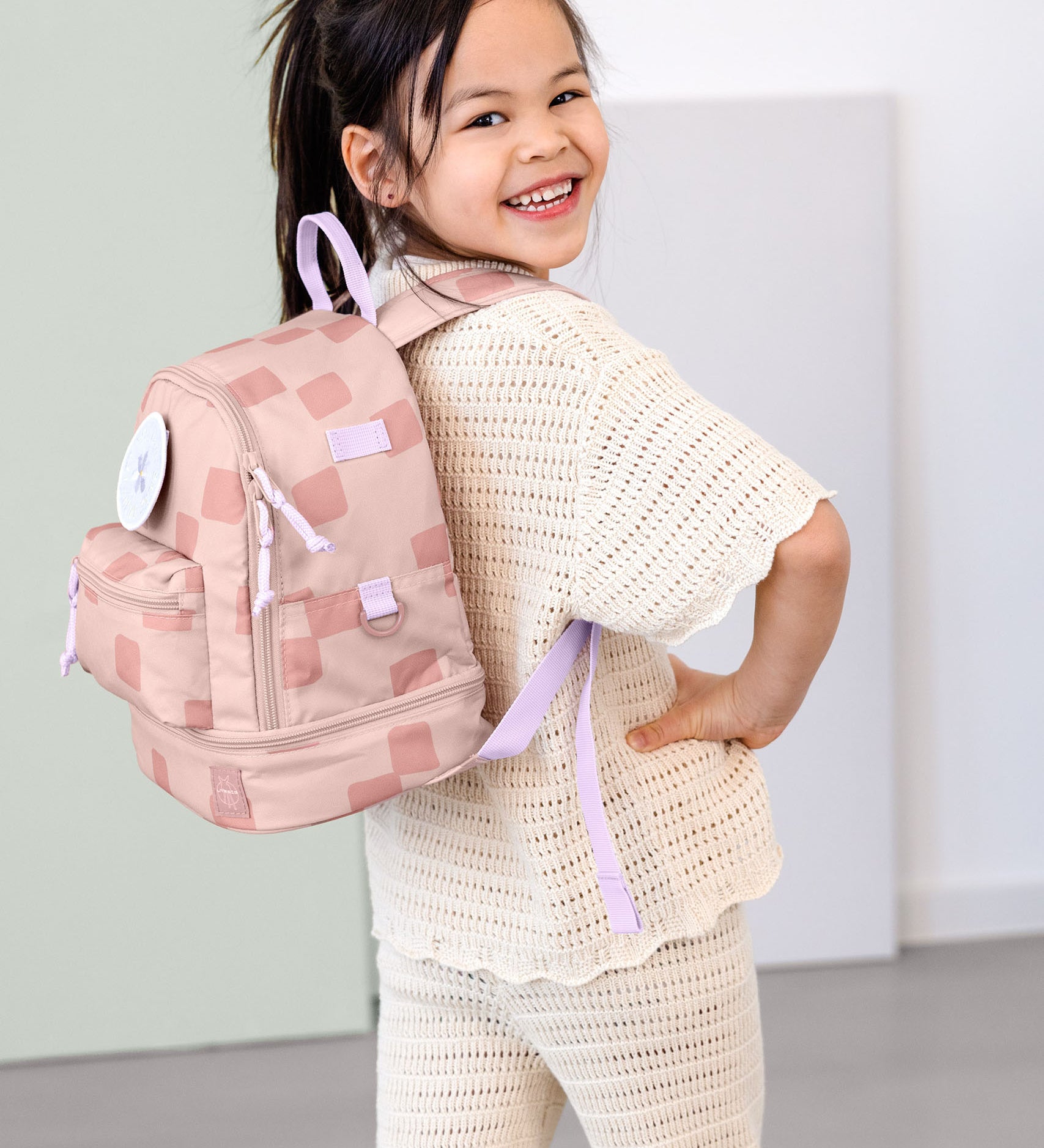 A child posing and wearing the Lassig kids mini pattern party rose pattern backpack.