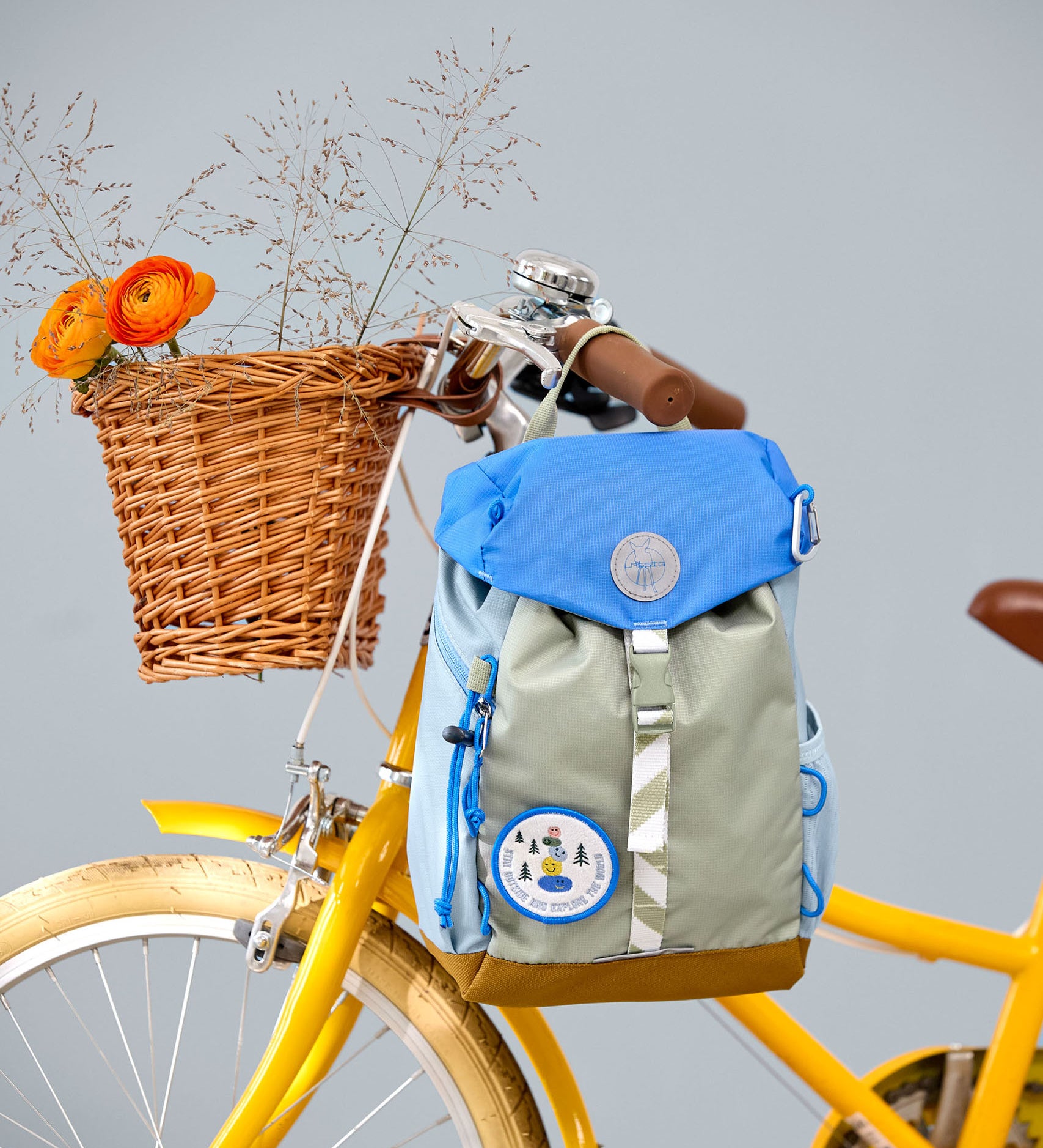 Lassig kids mini outdoor backpack in sunny explorer green hanging on a yellow bicycle. 