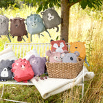 The Lassig 'About Friends' kids tiny backpack range, all laid out on a bench and hanging on a string in a garden. There are many different animal backpacks.