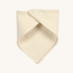 The Lassig organic cotton muslin bandana dribble bib, in a creamy Vanilla colour, with little push-in metal fastenings at the neck.