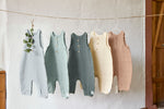 5 different coloured Lassig organic cotton muslin jumpsuits, hanging on a string of twine. 
