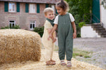 Two children wearing Lassig organic cotton muslin jumpsuits outside on a farm. 