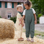 Two children wearing Lassig organic cotton muslin jumpsuits outside on a farm. 