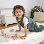 A toddler playing with wooden blocks, wearing the Lassig organic cotton baby jumpsuit romper. 