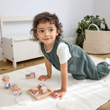 A toddler playing with wooden blocks, wearing the Lassig organic cotton baby jumpsuit romper. 