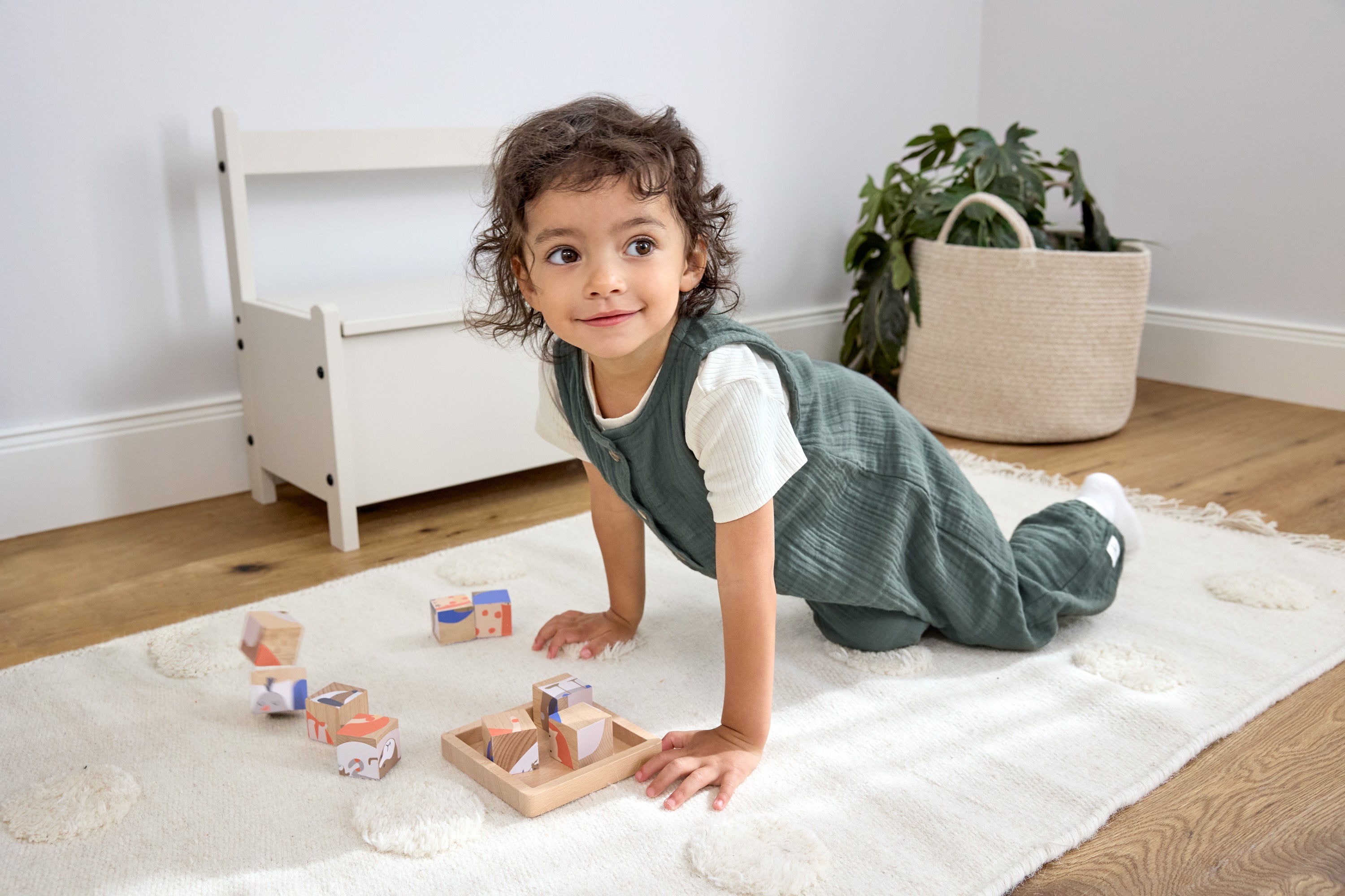A toddler playing with wooden blocks, wearing the Lassig organic cotton baby jumpsuit romper. 