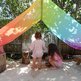 Children playing underneath Laura's play cotton large bright rainbow play cloths in bright rainbow in the garden