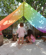 Children playing underneath Laura's play cotton large bright rainbow play cloths in bright rainbow in the garden