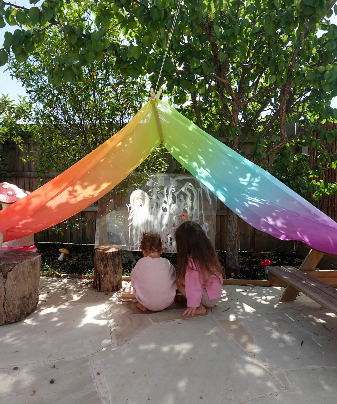 Laura's play cotton large bright rainbow play cloths in bright rainbow as a shelter with children playing underneath