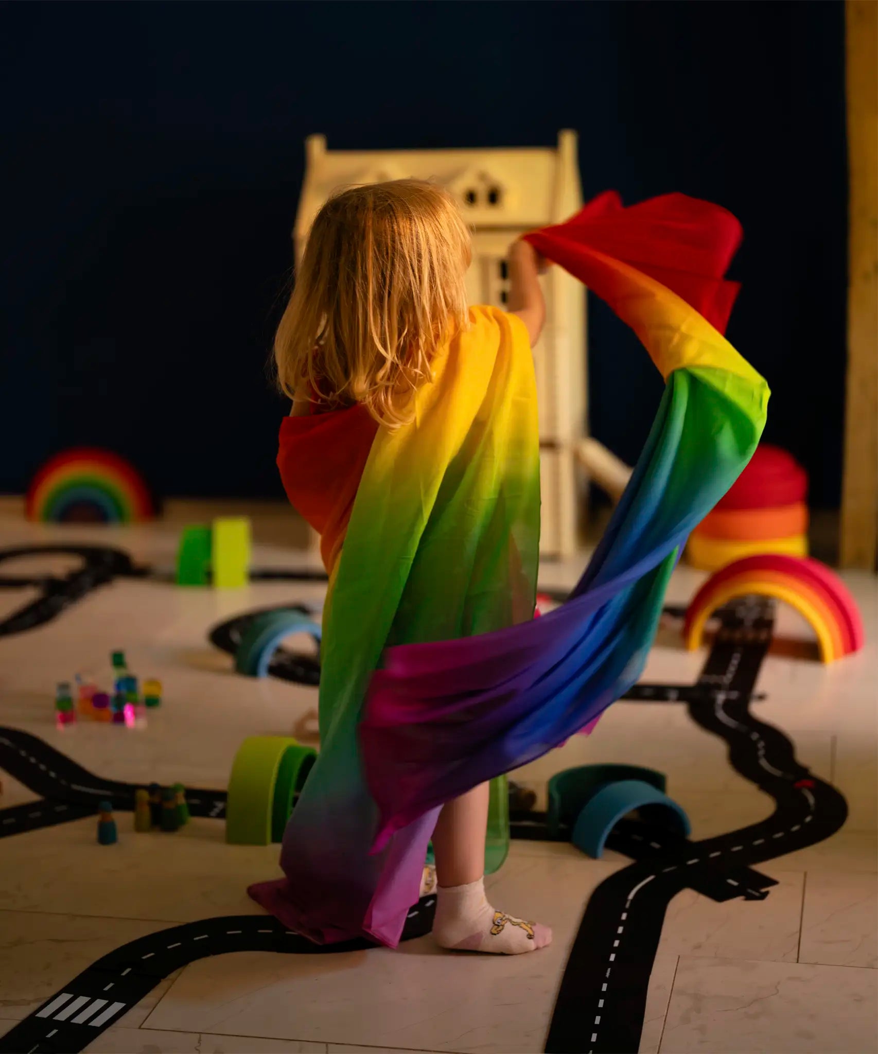 Child playing with Laura's play cotton large bright rainbow play cloths in a playroom 