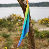 Laura's play cotton bright rainbow play cloths made from organic cotton tied onto a branch with a river in the background