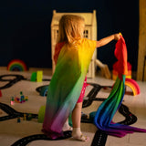 Child wearing with Laura's play cotton bright rainbow play cloths on the back and playing in a playroom 