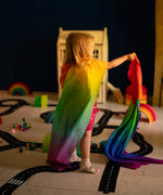 Child wearing with Laura's play cotton bright rainbow play cloths on the back and playing in a playroom 