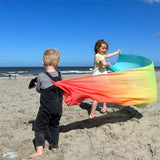 Children playing with Laura's play cotton large pastel rainbow play cloth on the beach