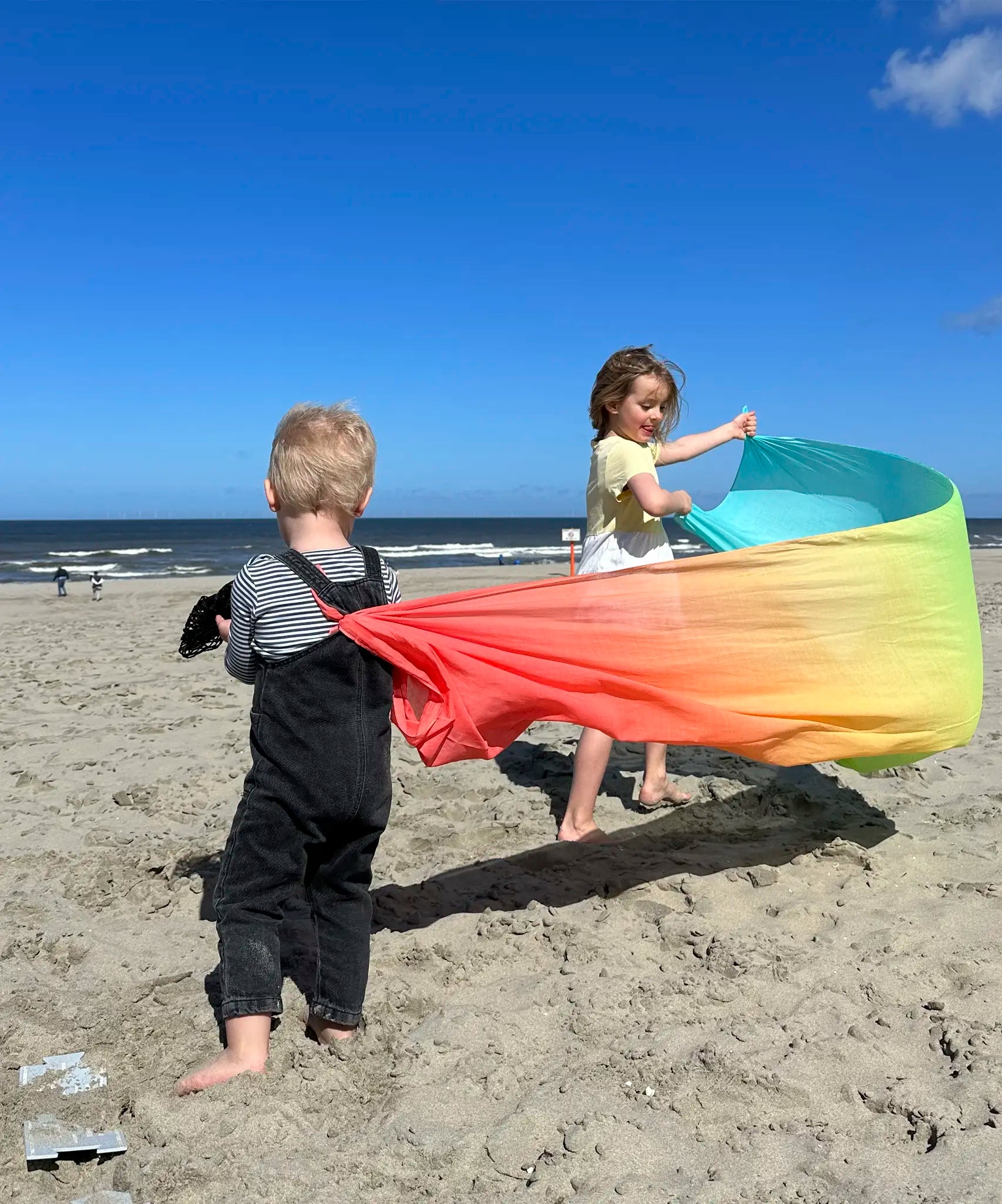 Children playing with Laura's play cotton large pastel rainbow play cloth on the beach