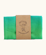 Laura's 100% organic cotton small play cloth in a green gradient held together by a decorated cardboard strip
