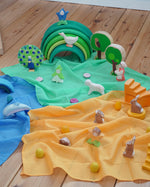 Laura's Play Cotton Play Cloths in blue, green and orange used in a small world play scene with Ostheimer figures and a green Grimm's rainbow in the Babipur playroom.