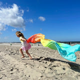 Child playing with Laura's play cotton large pastel rainbow play cloth on the beach