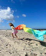 Child playing with Laura's play cotton large pastel rainbow play cloth on the beach