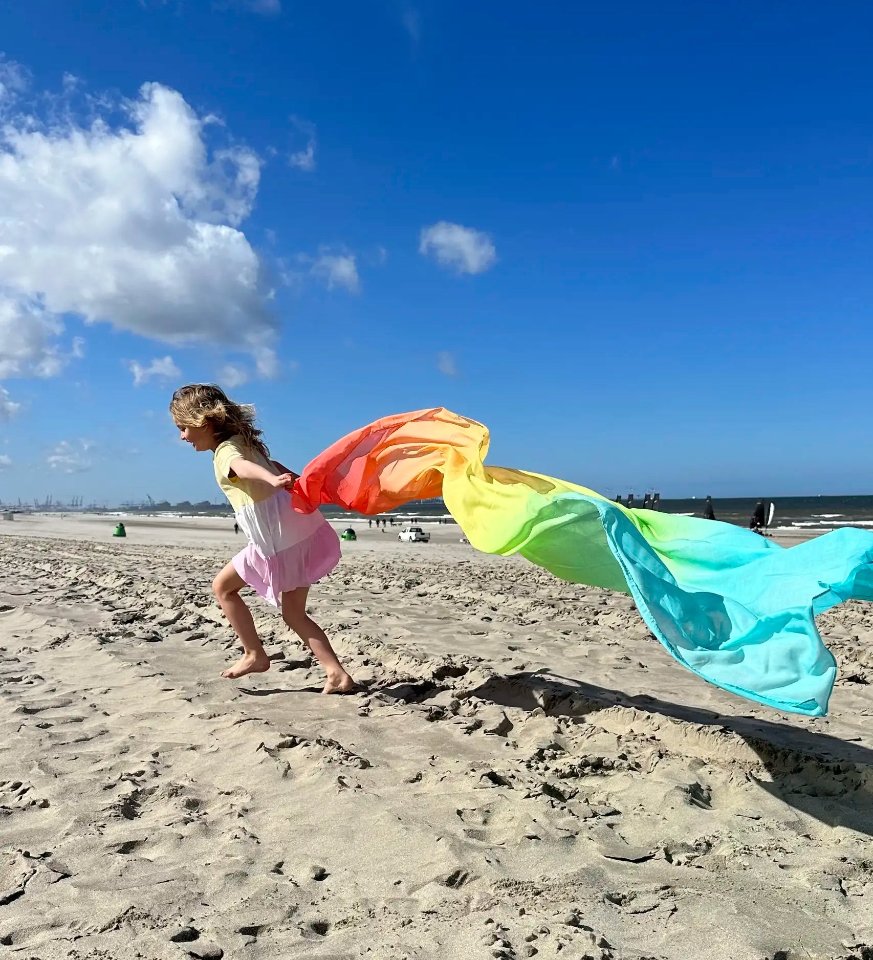 Child playing with Laura's play cotton large pastel rainbow play cloth on the beach