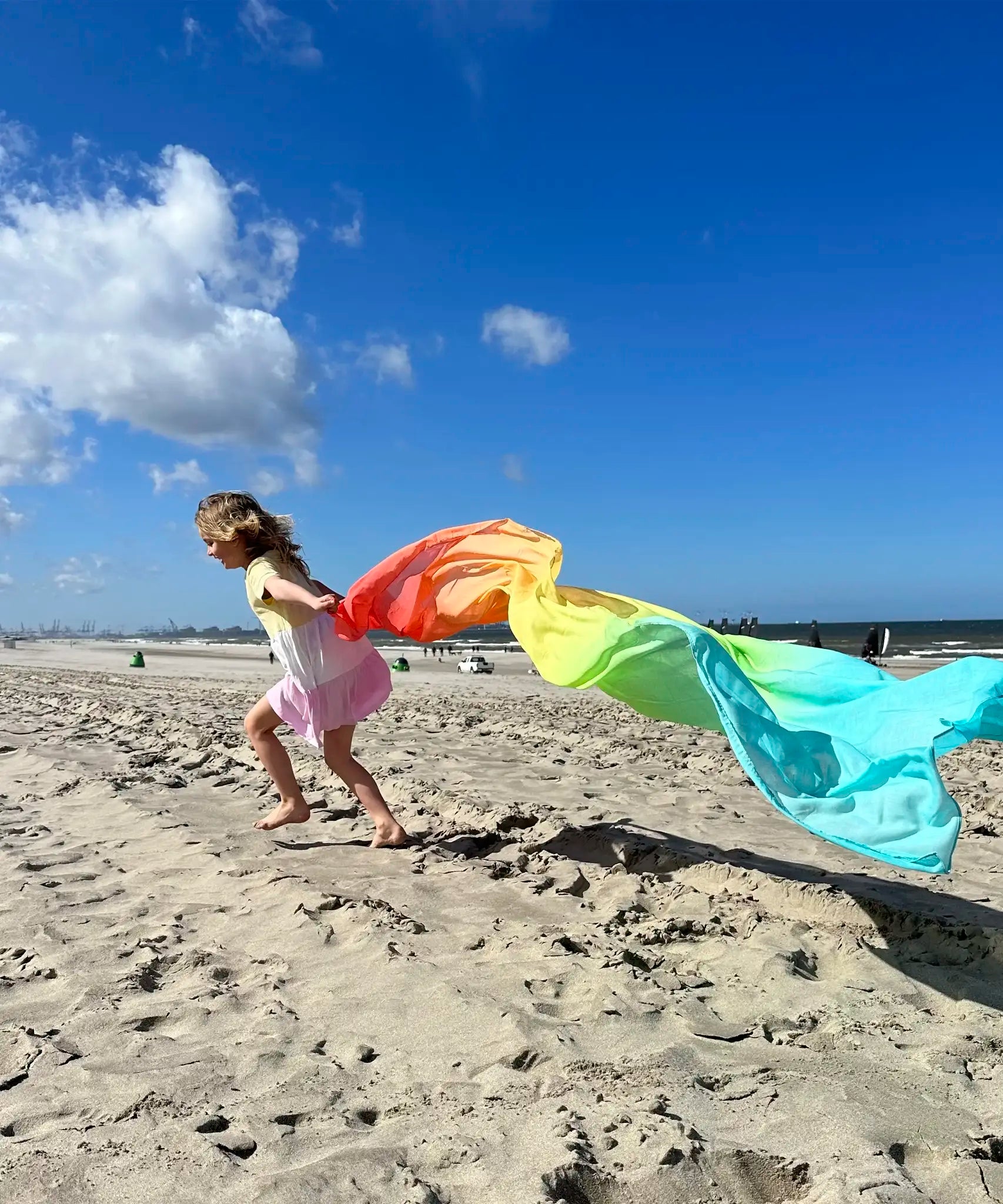 Child playing with Laura's play cotton large pastel rainbow play cloth on the beach