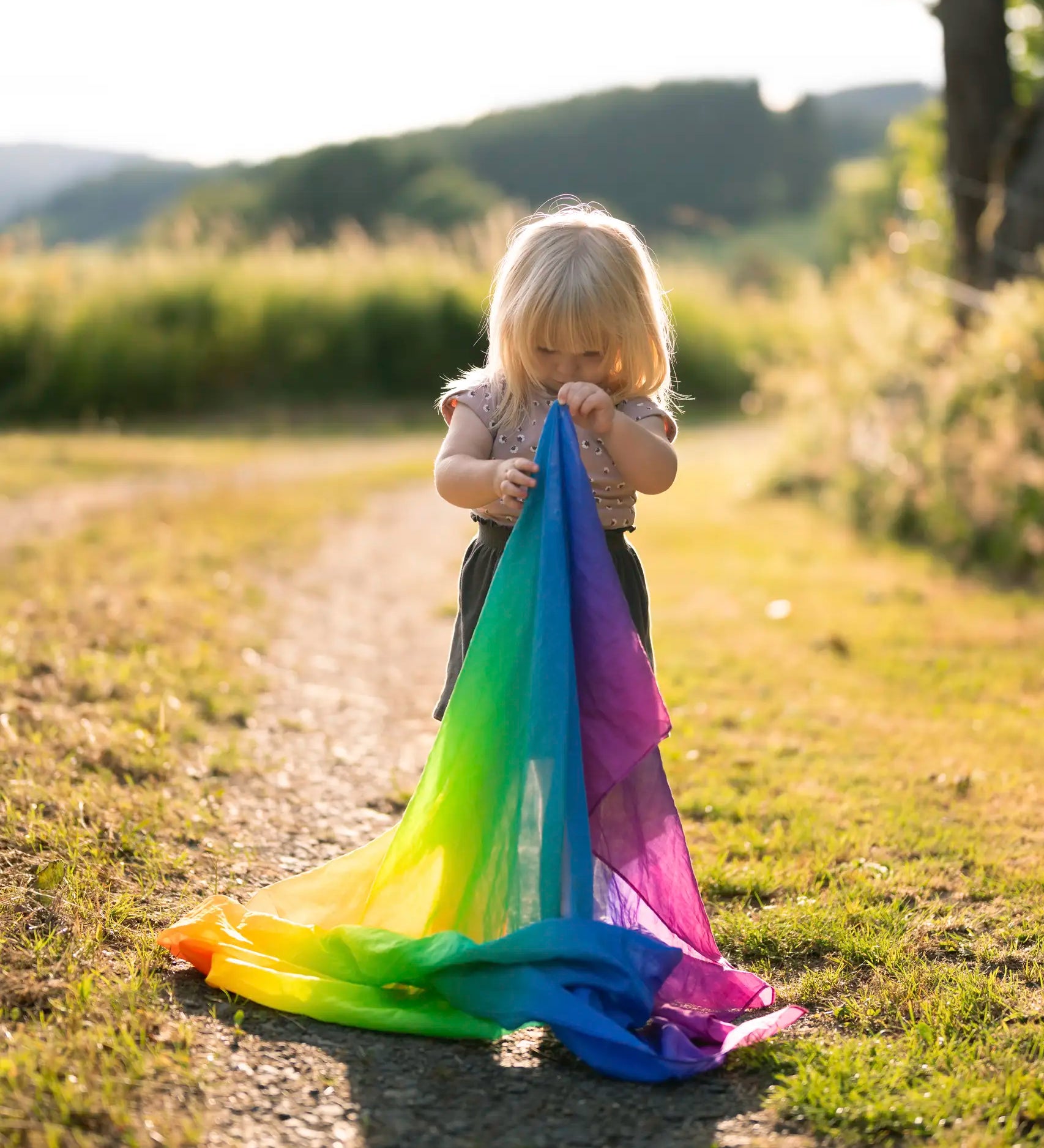 Child holding a Laura's play cotton rainbow cloth made from organic cotton in a grassy field