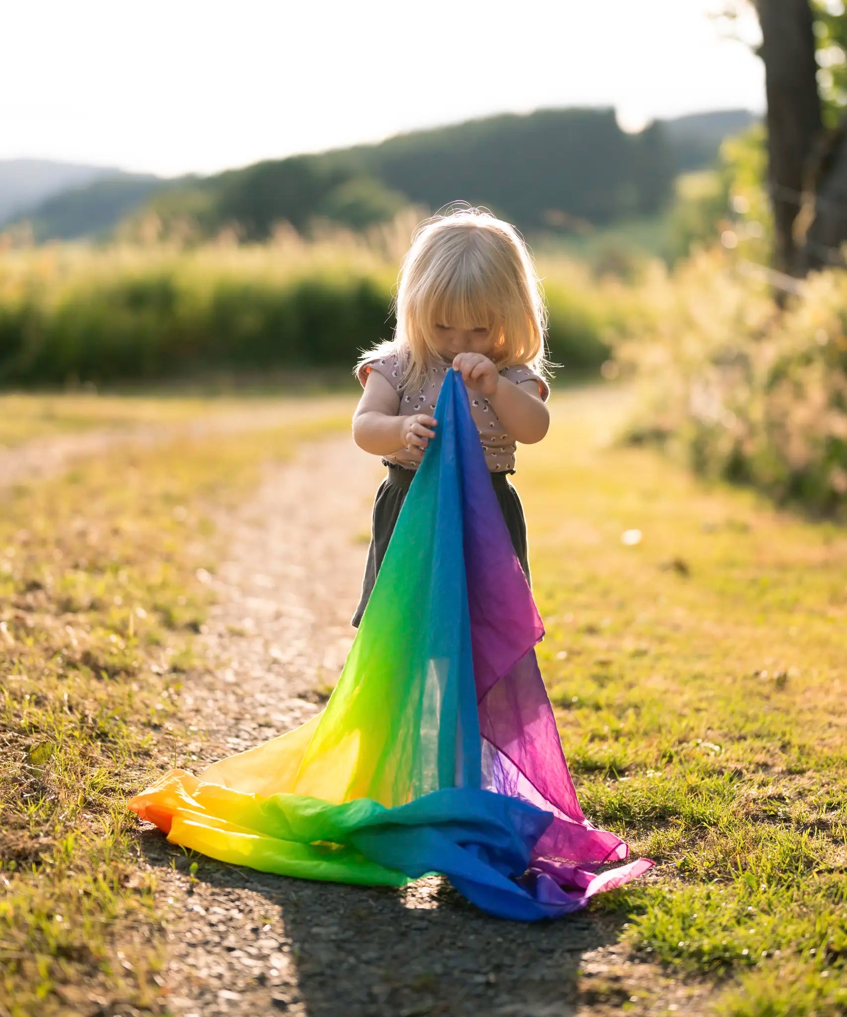 Child holding a Laura's play cotton rainbow cloth made from organic cotton in a grassy field