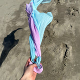 Adult hand holding Laura's organic cotton play cloths in light blue and violet on the beach
