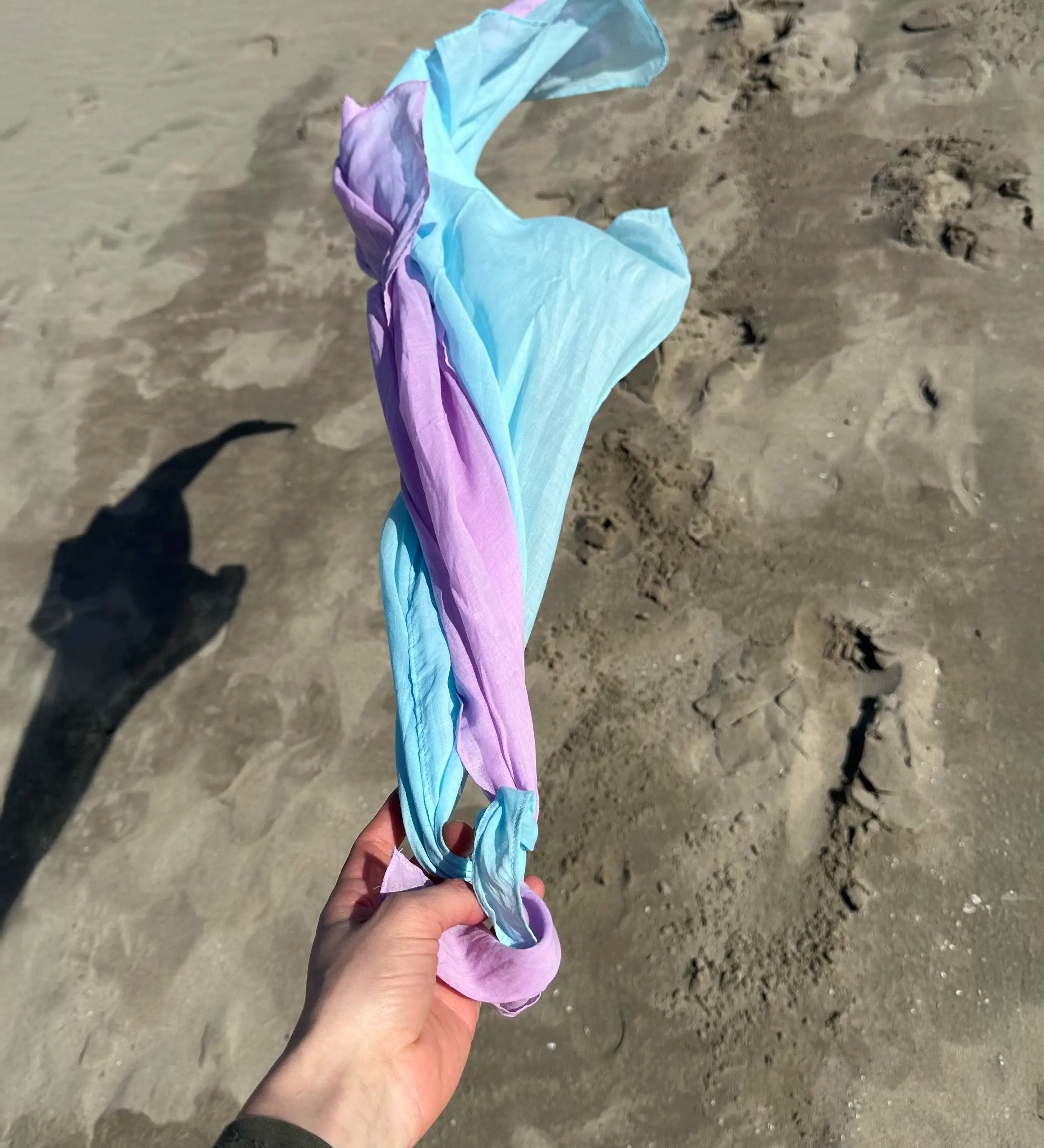 Adult hand holding Laura's organic cotton play cloths in light blue and violet on the beach