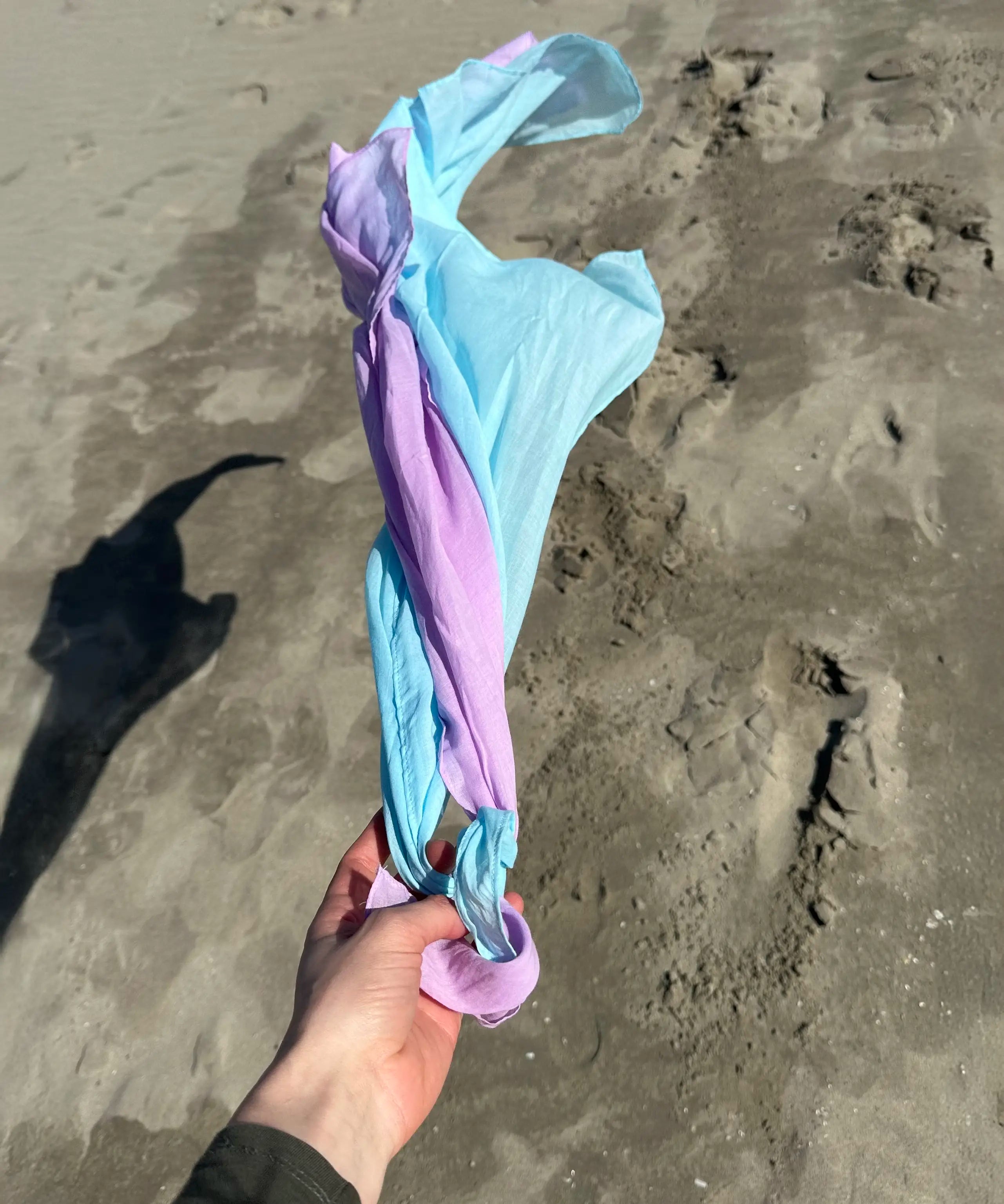 Adult hand holding Laura's organic cotton play cloths in light blue and violet on the beach