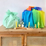 Light green and a rainbow 100% organic cotton play cloths wrapped around gifts standing on a wooden cabinet with a display