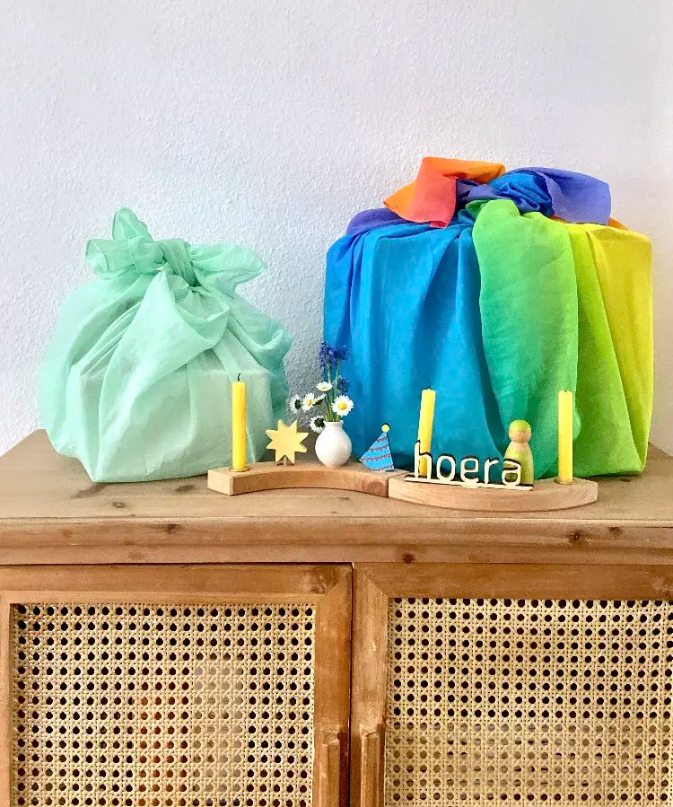 Light green and a rainbow 100% organic cotton play cloths wrapped around gifts standing on a wooden cabinet with a display