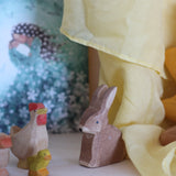 100% organic cotton yellow play cloth hanging over a wooden rabbit, hen and chick figure