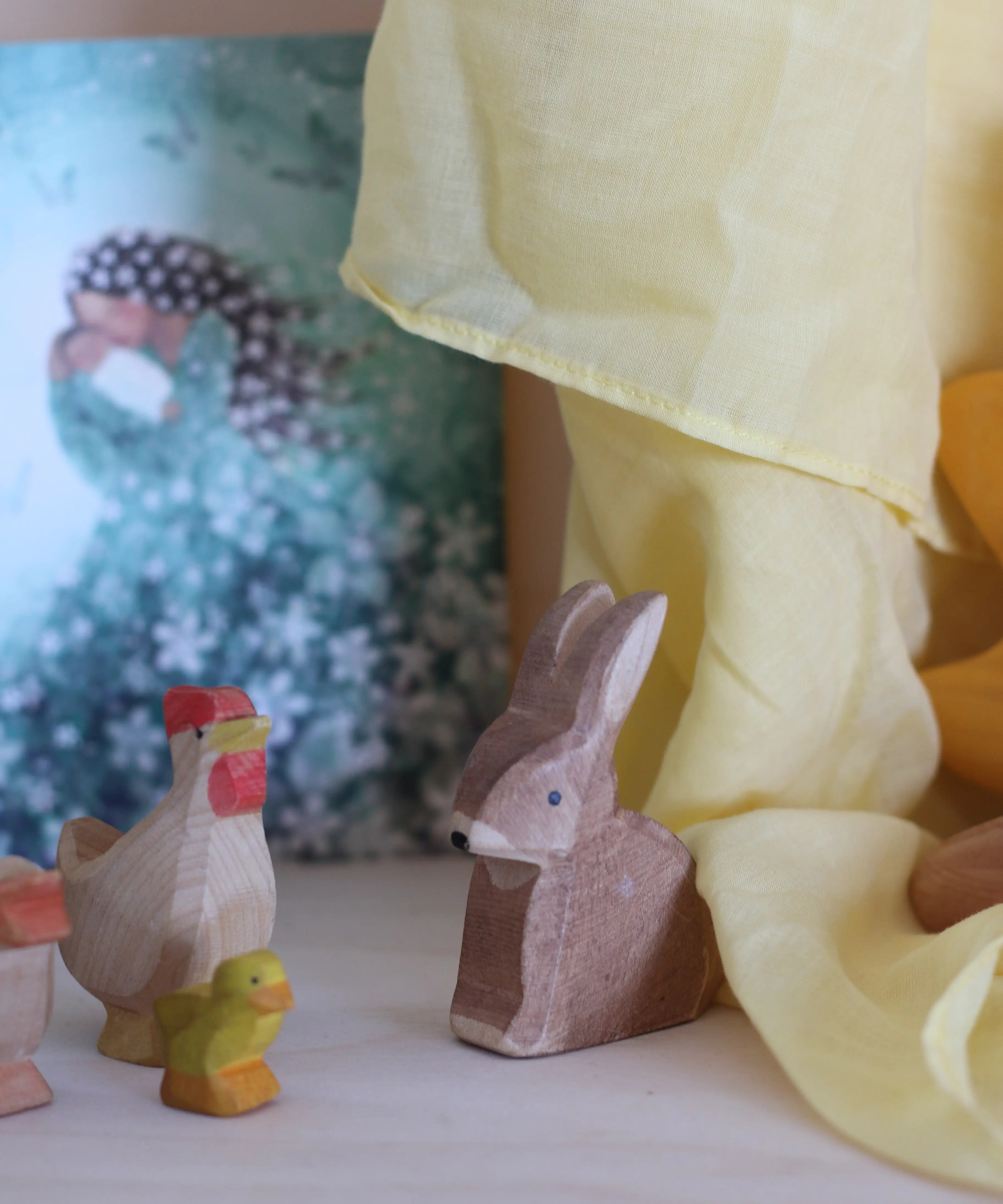 100% organic cotton yellow play cloth hanging over a wooden rabbit, hen and chick figure