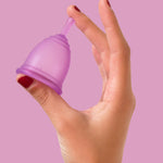 A person holding the Purple Silicone, BPA free and latex free Ruby Cup in between their fingers on a pink/purple background.