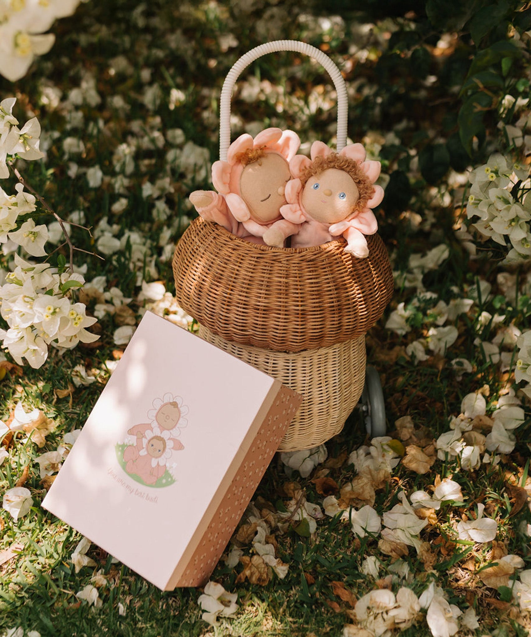 Olli Ella Limited Edition Blossom Buds Gift Set - Tulip showing Dozy Dinkum - Talia Tulip & Dinky Dinkum Doll - Tessa Tulip sat inside an Olli Ella basket on a flowery setting, with the packaging box lent against the basket