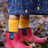 A child standing on wet leaves and wearing the Little Green Radicals ankle wellington boots