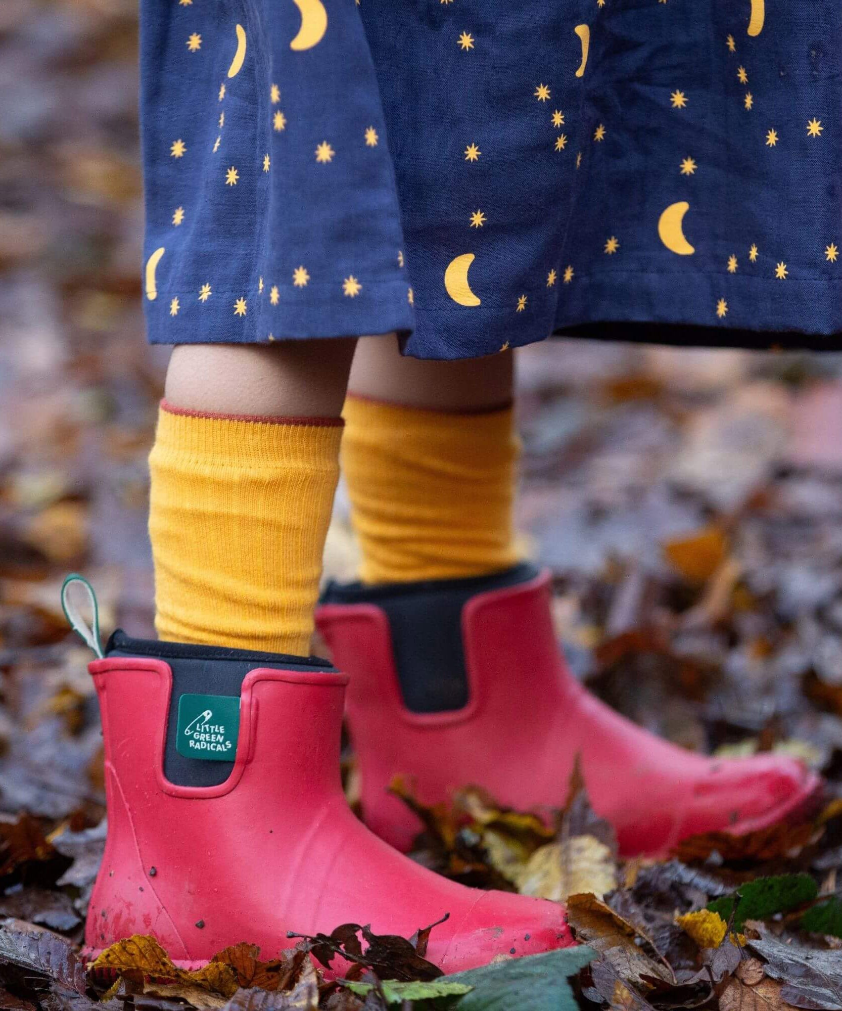 A child standing on wet leaves and wearing the Little Green Radicals ankle wellington boots